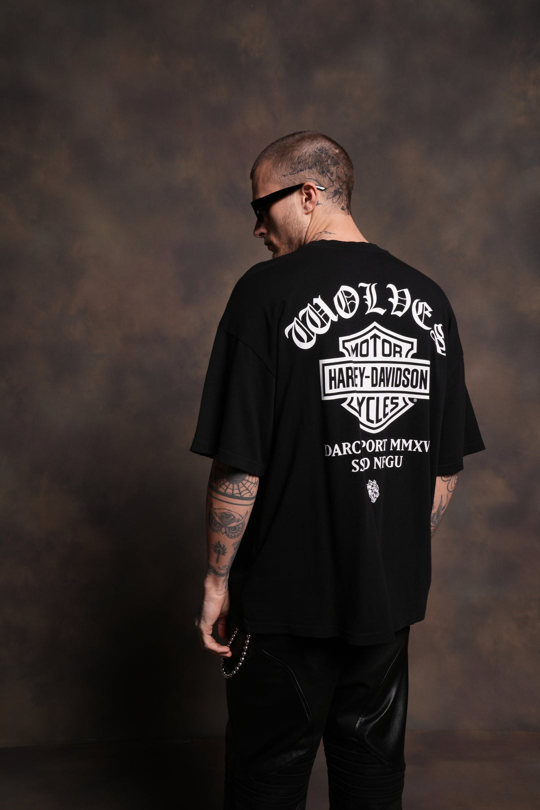 Person wearing a black t-shirt with 'Wolves Motor Harley Davidson' logo on the back against a brown textured background.